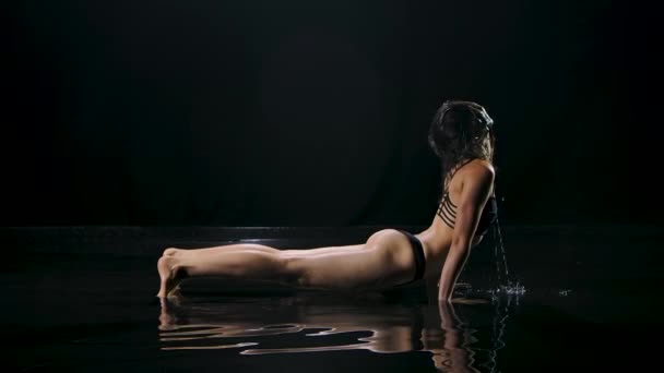 下向きの犬のヨガの位置を練習陸上の若い女性。水面の暗いスタジオで撮影。健康の概念のためのヨガスポーツ。黒の背景。スローモーション. — ストック動画
