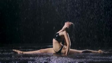 Yağmurun altında, genç bir kadın sicimin üzerine oturur ve egzersizin tadını çıkarır. Stüdyo ışığı suyun yüzeyinde parıltı yaratır. Yoga meditasyonu Asana 'yı gerer. Yavaş çekim.