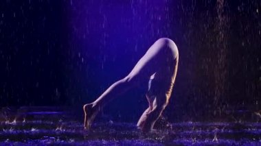 Sportif kadın stüdyo mavi ışığı ve su yağmuru ile ileri tribünde duruyor. Damlalar içinde bir kadın cesedi. Resim stüdyoda siyah bir arkaplanda çekildi. Yavaş çekim.