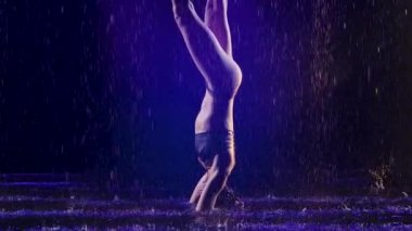 Sportif kadın stüdyo mavi ışığı ve su yağmuru ile ileri tribünde duruyor. Damlalar içinde bir kadın cesedi. Resim stüdyoda siyah bir arkaplanda çekildi. Yavaş çekim.