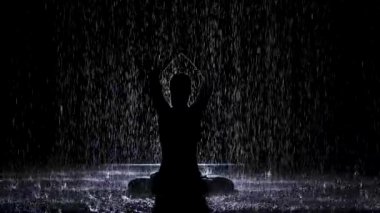 Nilüfer pozisyonunda katlanmış ellerle yağmur derelerinin altında bir siluet belirir. Siyah arkaplan ve neon ışığı. Yavaş çekim.