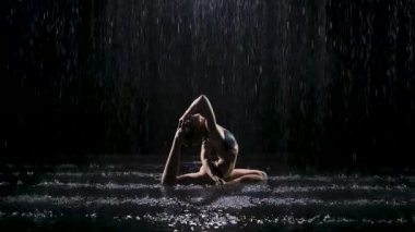 Kumruda siyah saçlı güzel genç bir kadın yağmur derelerinin altında poz veriyor. Stüdyo ışığı suyu yansıtır ve parlar. Siyah arka planda karanlık bir stüdyoda çekilmiş. Yavaş çekim.