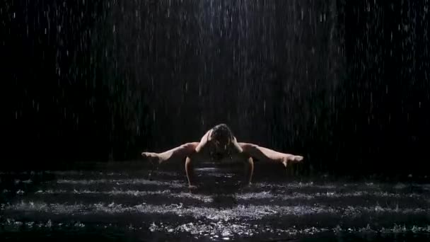 雨の流れの中で、若い女性が握手をする。黒を背景にスタジオライトで濡れたスレンダーなボディが輝きます。スローモーション. — ストック動画