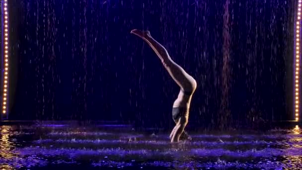 Hermosa mujer joven se encuentra en cabecera avanzada con estudio de luz azul y lluvia de agua. Cuerpo femenino en gotas de agua. Foto tomada en el estudio sobre fondo negro. Movimiento lento. — Vídeos de Stock