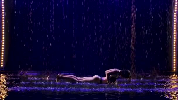 Υγρή γυναίκα εκτελεί ασκήσεις γιόγκα lunge με στούντιο μπλε φως και βροχή νερού. Θηλυκό σώμα σε σταγόνες νερού. Φωτογραφία τραβηγμένη στο στούντιο σε μαύρο φόντο. Αργή κίνηση. — Αρχείο Βίντεο
