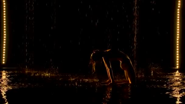 Silueta de mujer atractiva realizando pose puente. La luz amarilla cae suavemente sobre el cuerpo húmedo de una joven atractiva. Aqua studio con lluvia. Movimiento lento. — Vídeos de Stock