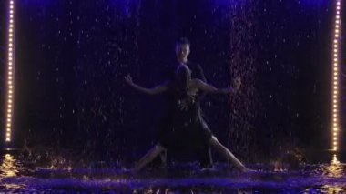 Tutkulu dans eden genç çiftin siluetleri yağmur altında stüdyoda hareket ediyor. Yavaş çekim.