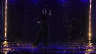 Yağmur altında Bachata dansı yapan bir adamın silueti. İnsan yağmur damlaları arasında suyun yüzeyinde dans eder. Neon ışıklı siyah arka plan. Yavaş çekim.