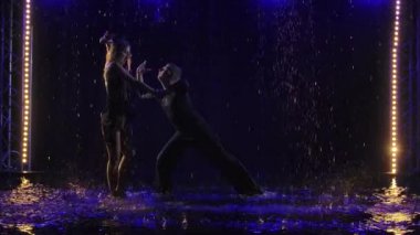 Genç ve güzel bir çift, dans ederken şehvetli bachata dansı yapıyor. Yağmur damlalarında hareket eden dansçıların siluetleri. Ayaklarına bir sürü küçük sprey sıçramış. Yavaş çekim.