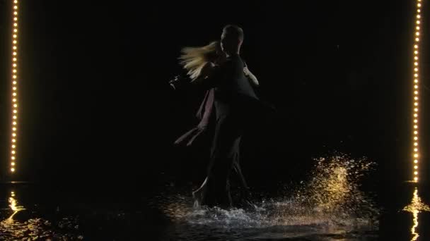 Bailarines de salón interpretando un elemento de bachata. Una silueta de una pareja bailando en la superficie del agua. Fondo negro con luz de escenario. Movimiento lento. — Vídeos de Stock