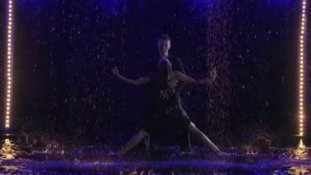 若いカップルの情熱的なダンスのバカータのシルエットは、注ぐ雨の中でスタジオで動きます。スローモーション. — ストック動画