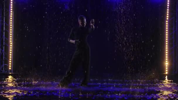 Силует чоловіка, що виконує елемент танцю бачати під дощем. Чоловік танцює на поверхні води серед дощів. Чорний фон з неоновими прожекторами. Повільний рух . — стокове відео