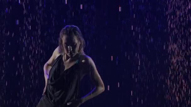 Sylwetka kobiety wykonującej element tańca bachaty wśród kropel deszczu. Czarne tło z niebieskim neonem reflektorów. Zwolnij trochę. Zamknij się.. — Wideo stockowe
