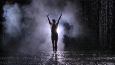 Yağmur damlaları arasındaki dumanın içinde erotik, çağdaş bir dans. Genç bir kadın suyun yüzeyinde sorunsuzca hareket ederek birçok sıçrama oluşturur. Koreografiyi düşün. Yavaş çekim.