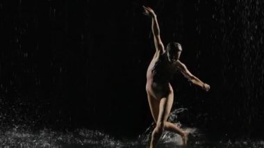 Dar bej mayo giymiş ıslak genç bir kadın yağmurun altında yerde dans ediyor ve su damlatıyor. Su damlaları, yağmur, modern dans. Ağır çekim. Kapat..