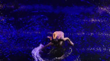 Yağmurun altında zarif dans figürleri sergileyen zarif genç dansçı manzarası. Şefkatli kadın sanatçı, siyah arka planda modern düşünce ve mavi arka planda dans ediyor. Ağır çekim. Kapat..