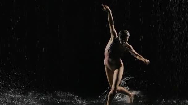 Мокра молода жінка в жорсткому бежевому купальнику танцює на підлозі під дощем і бризкає воду. Краплі води, дощ, сучасний танець. Повільний рух. крупним планом . — стокове відео