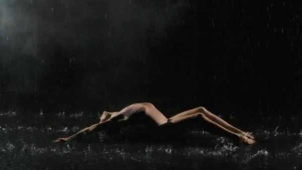 タイトなベージュの水着でぬれた若い女性が雨の下で床の上で踊っていると水のスプラッシュ。水、雨、現代舞踊をドロップします。スローモーション。閉じろ!. — ストック動画