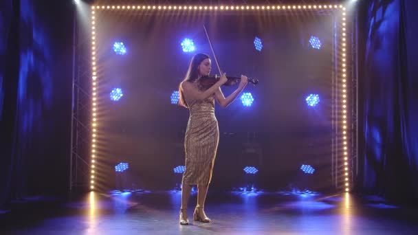 Ung brunett spelar fiol i en studio med klarblått neonljus. Långsamma rörelser. — Stockvideo