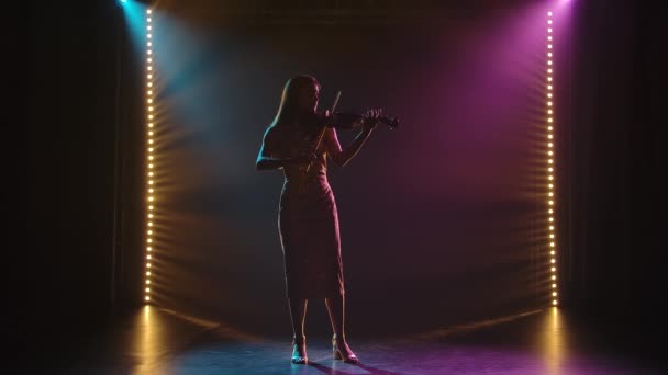 Giovane musicista magistralmente suona il violino in studio. Silhouette di una figura femminile su uno sfondo fumoso con illuminazione al neon. Rallentatore. — Video Stock