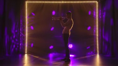 Heyecanla trompet çalan bir adamın yan görüntüsü. Dinamik renkli ışıkları olan koyu bir arka planda erkek silueti. Yavaş çekim.