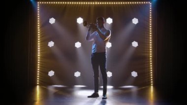 Stüdyodaki profesyonel bir trompetçinin tek başına neon ışıklarının arka planına karşı performansı. Yavaş çekim.