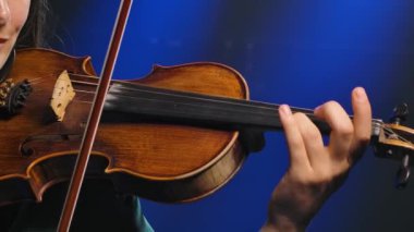 Profesyonel keman çalıyor. Genç bir kadın müzisyenin elindeki yakın çekim enstrümanı. Yavaş çekim.