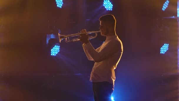 Een zijaanzicht van een professionele trompettist. Opgenomen in een rokerige donkere studio met dynamische veelkleurige lichten. Langzame beweging. Sluiten.. — Stockvideo