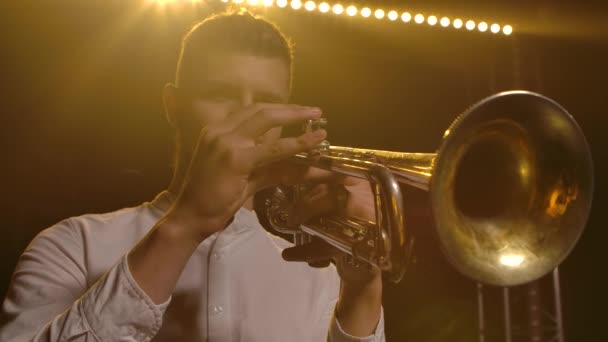 Detail van een mensenhand die trompet speelt. Mannelijke muzikant optredend tegen een rokerige gele achtergrond met achtergrondverlichting. Langzame beweging. Sluiten.. — Stockvideo