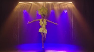 Sarı bir karnaval kostümü içinde dans eden muhteşem genç bir kadın. Bir bayan dansçı, mavi arka planı olan bir stüdyoda hareketlerin zarafetini gösterir. Yavaş çekim.