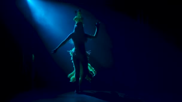 Eine hübsche junge Frau in verführerischem Faschingskostüm und Federkopfschmuck tanzt aufbrausend. Silhouette auf schwarzem Hintergrund. Zeitlupe. — Stockvideo