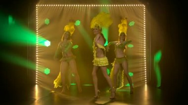Ateşli kadın dansçılar üçlüsü Brezilya karnaval kostümleriyle dans ediyor. Dinamik neon ışıkları olan tiyatro kadın dans gösterisi. Yavaş çekim.