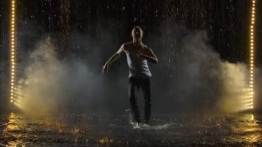 Şiddetli yağmurda dans eden erkek dansçı. Islak elbiseli bir adamın siluetleri danstan zevk alıyor. Yavaş çekim.