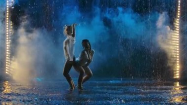 Yağmur damlaları ve dumanda tutkuyla dans eden iki genç kadın. Islak elbiseli kadın siluetleri yavaş çekimde erotik hareket eder..