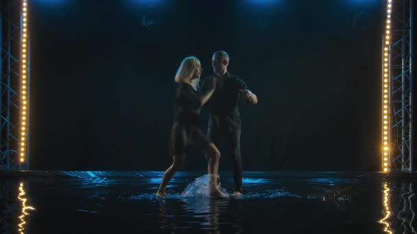 Hermosa pareja bailando baile latino. Bailarines profesionales bailan salsa en la superficie del agua. Estudio oscuro retroiluminado. Movimiento lento. — Vídeos de Stock