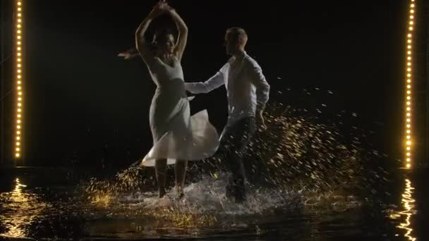 Пара танцующих сальс. Страстный горячий красивый танец, исполненный в темной студии на водной поверхности со множеством всплесков. Медленное движение. — стоковое видео
