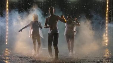 Profesyonel dansçılar karanlık dumanlı bir stüdyoda salsa yapıyorlar. Yağmurda ağır çekimde hareket eden üç cesedin siluetleri.
