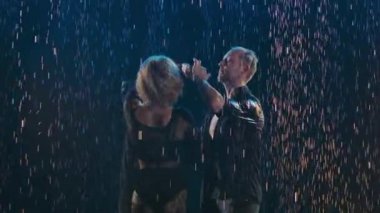 Olumlu yetişkin çiftler siyah arka planda yağmur damlalarında dans ediyorlar. Ağır çekim. Kapat..