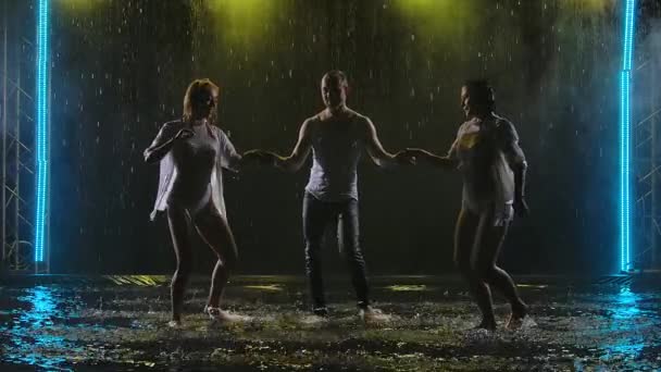 Bailarines profesionales realizan elementos de salsa en un estudio ahumado oscuro. Siluetas de tres cuerpos bajo la lluvia moviéndose en cámara lenta. — Vídeos de Stock