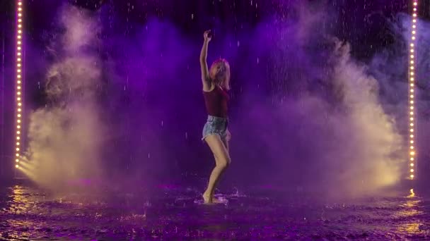 En våt blondin visar dansens element i regnet mot bakgrund av vackert studioljus och rök. Passionerad latinamerikansk dans i slow motion. — Stockvideo