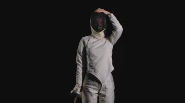 Profesyonel bir eskrim sporcusunun portresi koruyucu bir maske takıyor ve elinde kılıç ile dövüş pozisyonuna geçiyor. Siyah arka plan. Ağır çekim. Kapat..