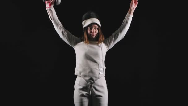 Πορτρέτο της αυτοπεποίθηση νεαρή γυναίκα ξιφομάχος. Μια αθλήτρια με λευκό κοστούμι με σπαθί στα χέρια φαίνεται ίσια και ποζάρει. Μαύρο φόντο. Αργή κίνηση. Κλείσε.. — Αρχείο Βίντεο