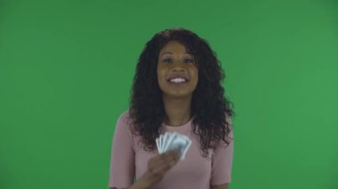 Güzel Afrikalı Amerikalı genç bir kadının portresi kameraya bakıyor ve mutlulukla ağlıyor ve gözyaşlarını dolarla siliyor. Yanan esmer, kot pantolonlu dalgalı saçlı ve bej bluzlu.