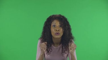 Güzel Afrikalı Amerikalı genç bir kadının portresi heyecanla kameraya bakıyor ve zafer zaferini kutluyor. Yanan esmer, kot pantolonlu dalgalı saçlı ve bej bluzlu.