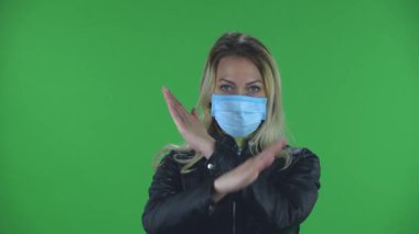 Tıbbi koruyucu yüz maskesi takmış güzel bir kadının portresi kameraya bakıyor ve ellerini çapraz yapıp X şeklini oluşturuyor bu da hayır ve dur demek oluyor. Sarışın ve gevşek