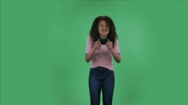 Güzel Afrikalı Amerikalı genç bir kadının portresi kameraya bakıyor ve neşeyle kablosuz kontrol cihazını kullanarak video oyunu oynuyor. Yanan esmer, dalgalı saçlı ve kot pantolonlu.