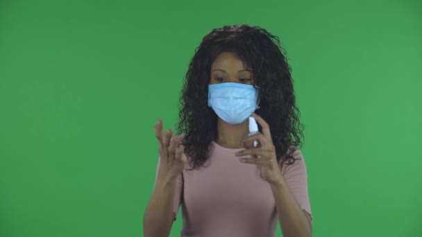 カメラを見て、コロナウイルスの拡散を防ぐために彼女の手に防腐剤を適用する医療保護顔マスクの美しいアフリカ系アメリカ人の若い女性の肖像画。燃焼 — ストック動画