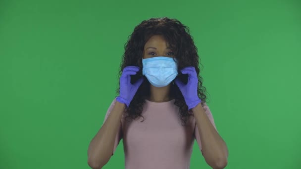 아름다운 아프리카계 미국인젊은 여성의 초상화가 의료용 마스크 숨결을 제거하고 웃고 있습니다. 스튜디오에 녹색 화면에 하얀 블라우스를 입고 긴 머리를 가진 붉은 머리 — 비디오