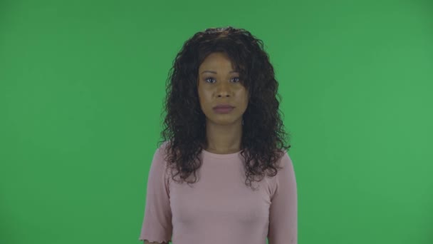 Ritratto di bella afroamericana giovane donna sta guardando la fotocamera con espressione del viso scioccato punti a qualcuno. Bruna bruciante con capelli ondulati in jeans e una camicetta beige su uno schermo verde — Video Stock