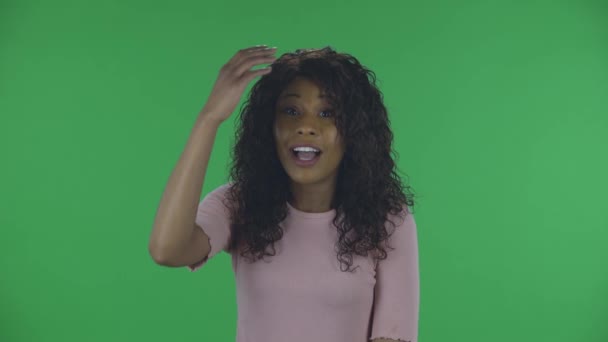 Portret pięknej afrykańskiej młodej kobiety jest zdenerwowany i sprawia, że twarz palmy. Płonąca brunetka z falowanymi włosami w dżinsach i beżową bluzką na zielonym ekranie w studio. — Wideo stockowe